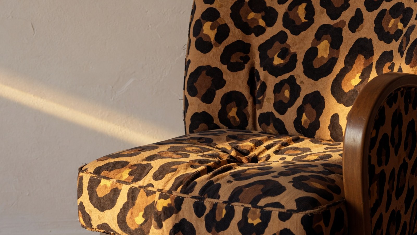 Fauteuil aux formes arrondies revêtu d'un tissu imprimé léopard en tons camel et marron, photographié en lumière rasante doré