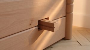 Gros plan détail d'une mortaise-tenon sur un lit enfant en bois de hêtre clair, éclairage rasant révélant le grain fin du boi
