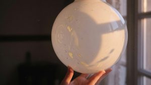 Gros plan d'une suspension vintage en verre opalin soufflé tenue contre la lumière d'une fenêtre, le verre laiteux brillant e