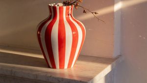 Vase en céramique blanc et rouge rayé, posé sur une étagère en marbre, éclairé par la lumière latérale.