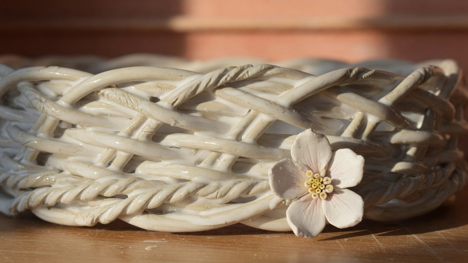 Gros plan d'une corbeille en céramique blanche aux brins d'argile tressés, avec petite fleur appliquée