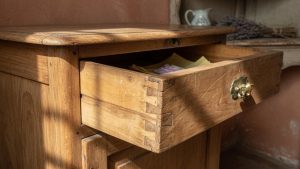 Gros plan du tiroir d'une coiffeuse ancienne, montrant l'assemblage à queue d'aronde et la patine dorée du bois.