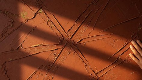 hero-1 Gros plan sur une surface d'enduit à la chaux teint terracotta, éclairage rasant révélant la texture et les reliefs du minera