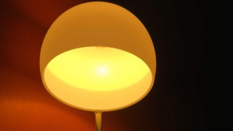 Lampe champignon en verre opalin illuminée, posée sur un buffet bois foncé, sa lumière créant une aura dorée sur le mur.