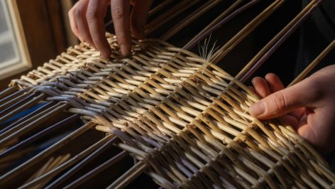 Gros plan des mains inspectant une vannerie en osier naturel dans un atelier, mettant en évidence les irrégularités et textur