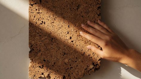 Gros plan panneau liège aggloméré contre mur, lumière rasante révélant pores et granules, tonalités miel à brun
