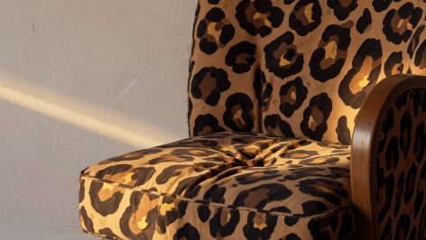 Fauteuil aux formes arrondies revêtu d'un tissu imprimé léopard en tons camel et marron, photographié en lumière rasante doré