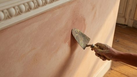Gros plan d'une surface de chaux fraîchement appliquée en teinte ocre-rose, texture minérale mate éclairée par la lumière ras