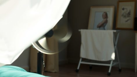 Étendoir à linge blanc avec drap ondulant devant ventilateur de bureau en métal, canapé velours vert en arrière-plan flou
