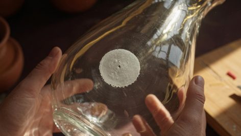 hero-6 Gros plan du dessous d'un vase en verre soufflé tenu par deux mains, révélant la cicatrice de pontil.