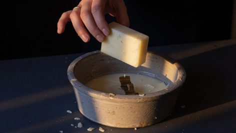 Bloc de cire soulevé au-dessus d'un pot en grès contenant une mèche et cire durcie.
